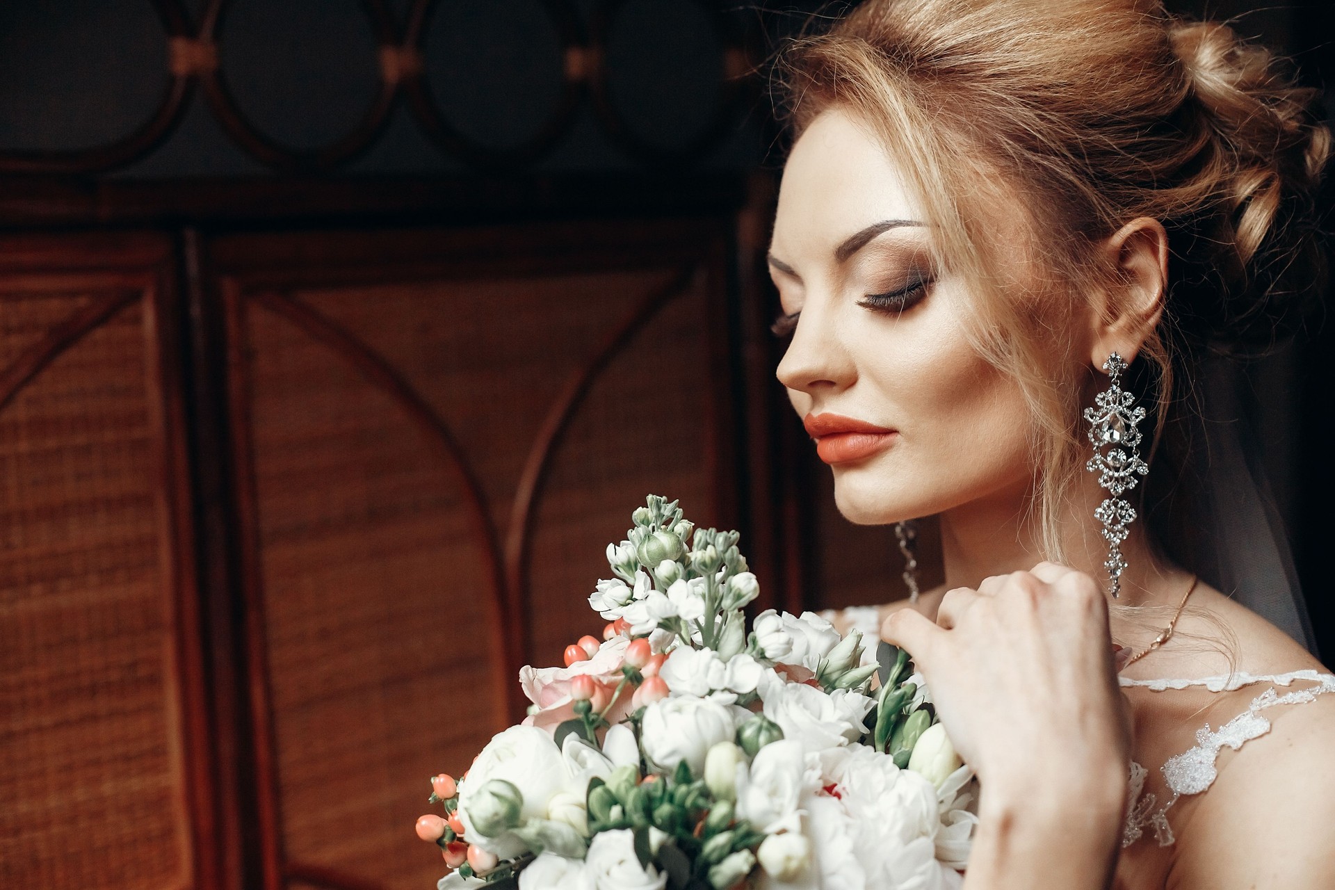 novia rubia elegante con bouquet moderno posando en luz de ventana en la mañana en el hotel. concepto de día de boda. Retrato de mujer hermosa con increíbles pendientes en vestido blanco